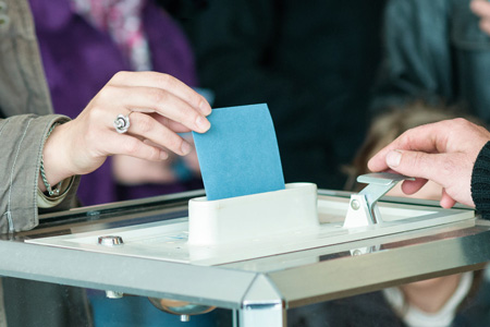 Main présentant un bulletin de vote à une urne