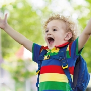 Un enfant heureux, qui lève les bras au ciel, avec un cartable