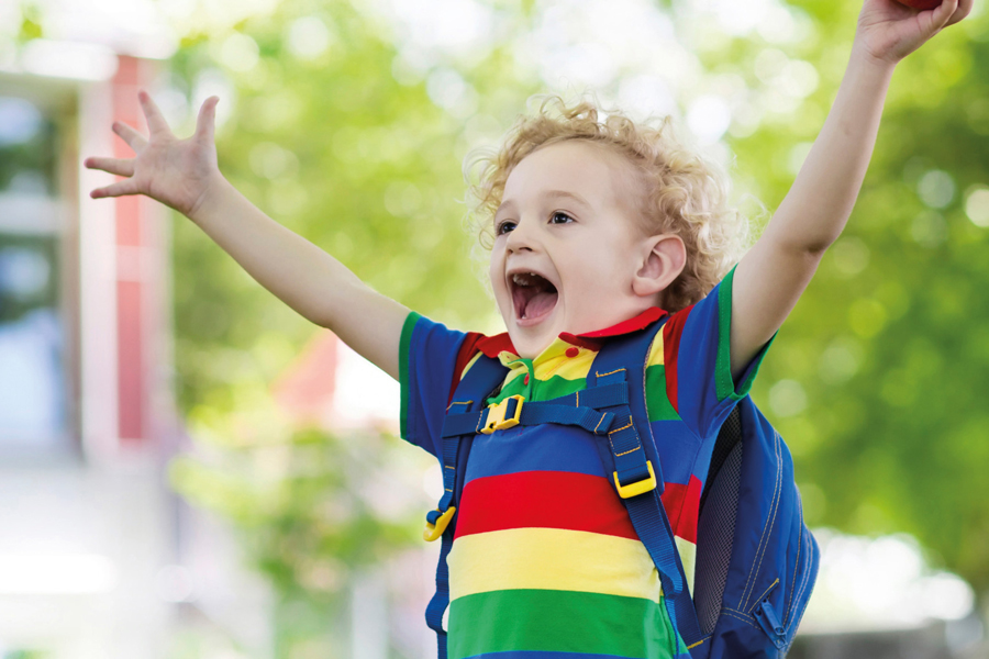 Un enfant heureux, qui lève les bras au ciel, avec un cartable